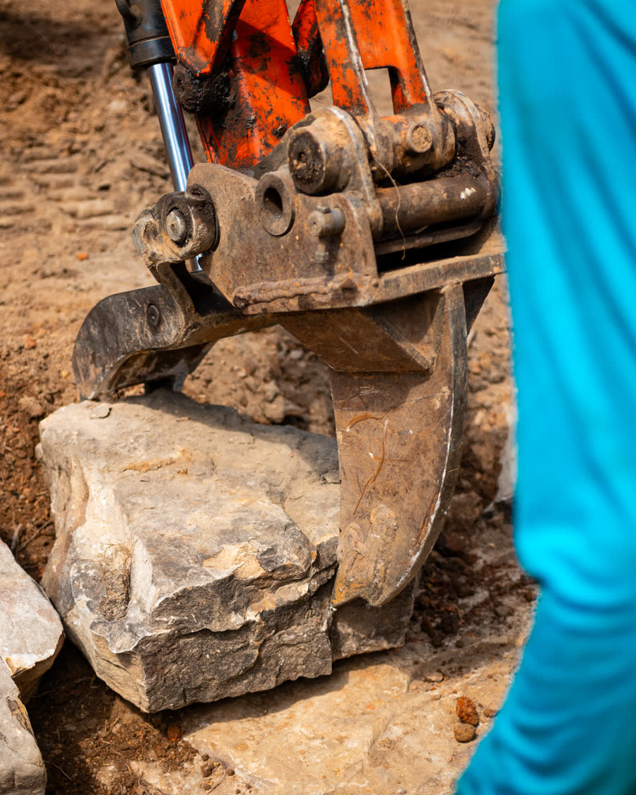 Close detail of an excavator bucket gripping a slab of stone