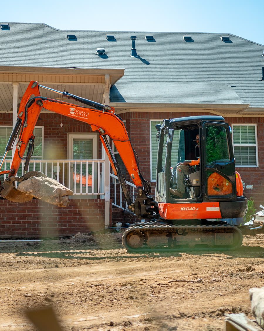 Excavator lifting a stone outside a brick home