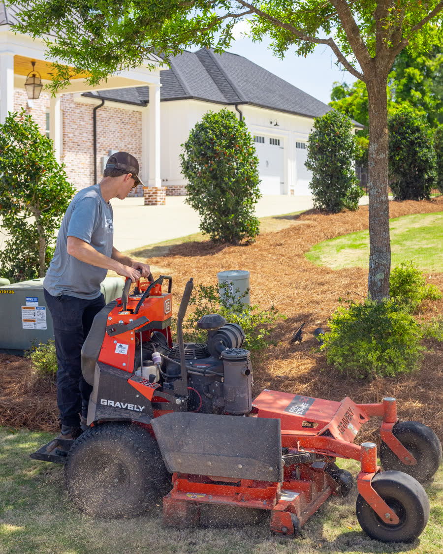 Stephens Lawn Care operator on a stand-on mower beside a home